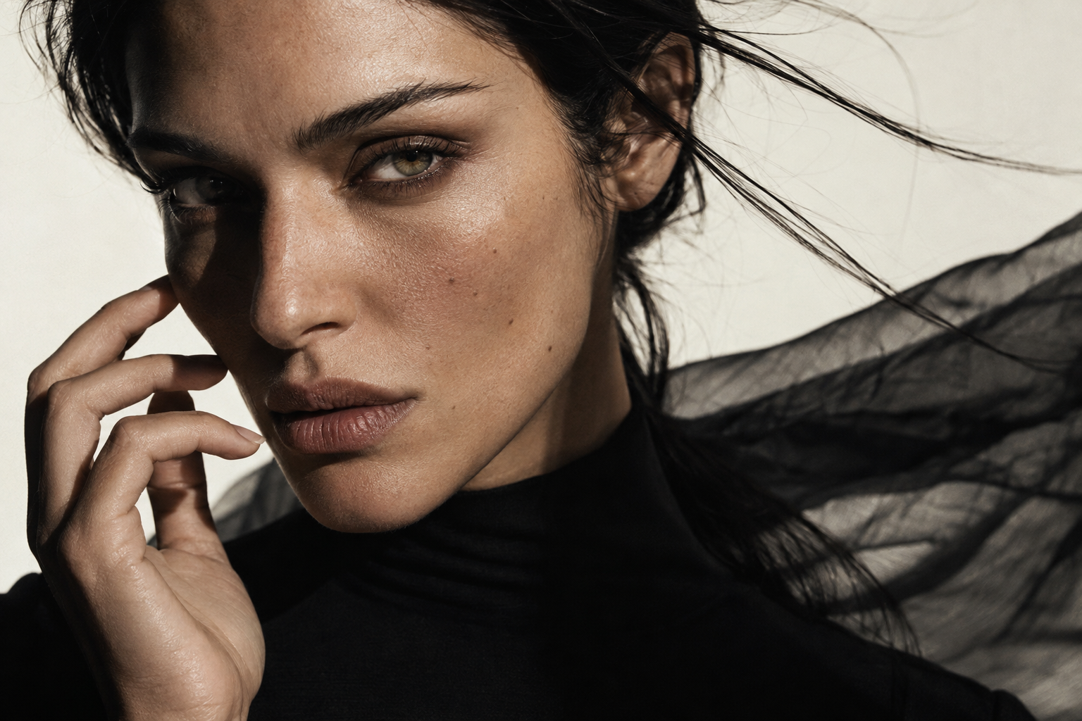 Close beauty portrait in sculptural light, with wind-swept dark hair and flowing black fabric.