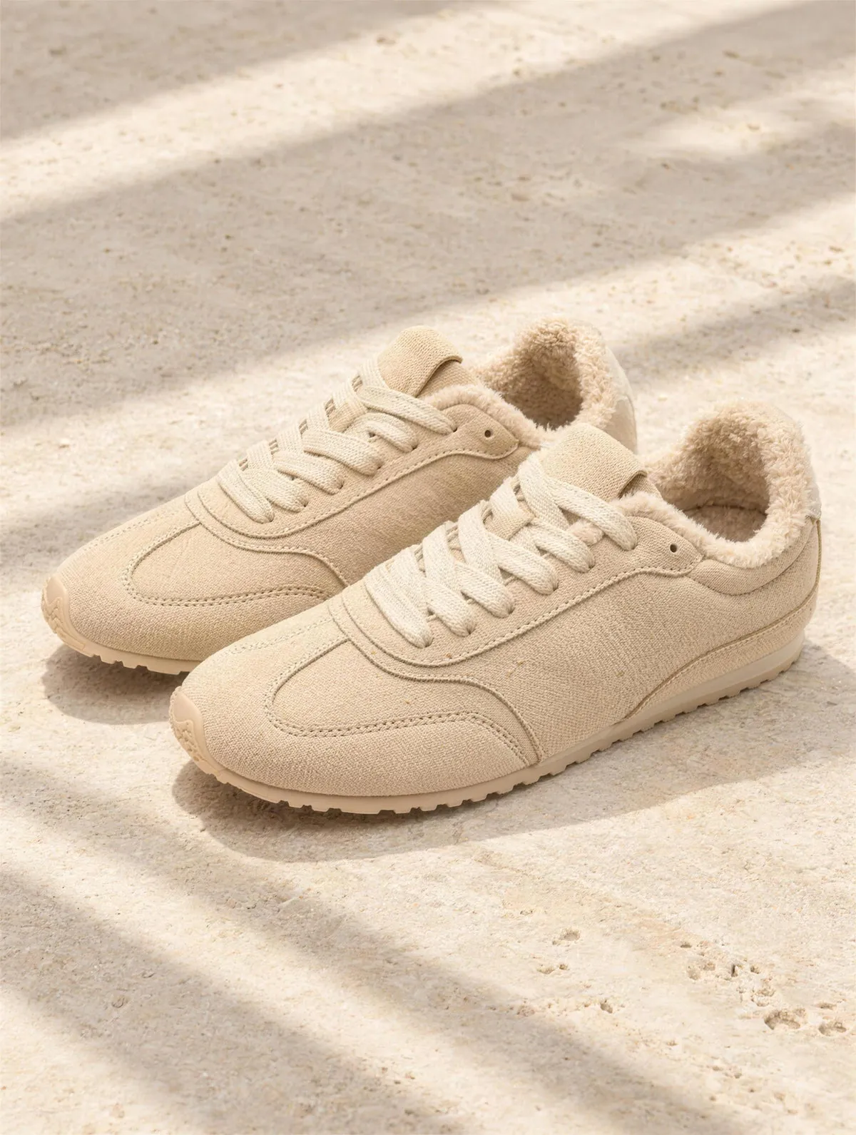 The Window Seat Sneaker in sand suede with shearling trim on limestone.